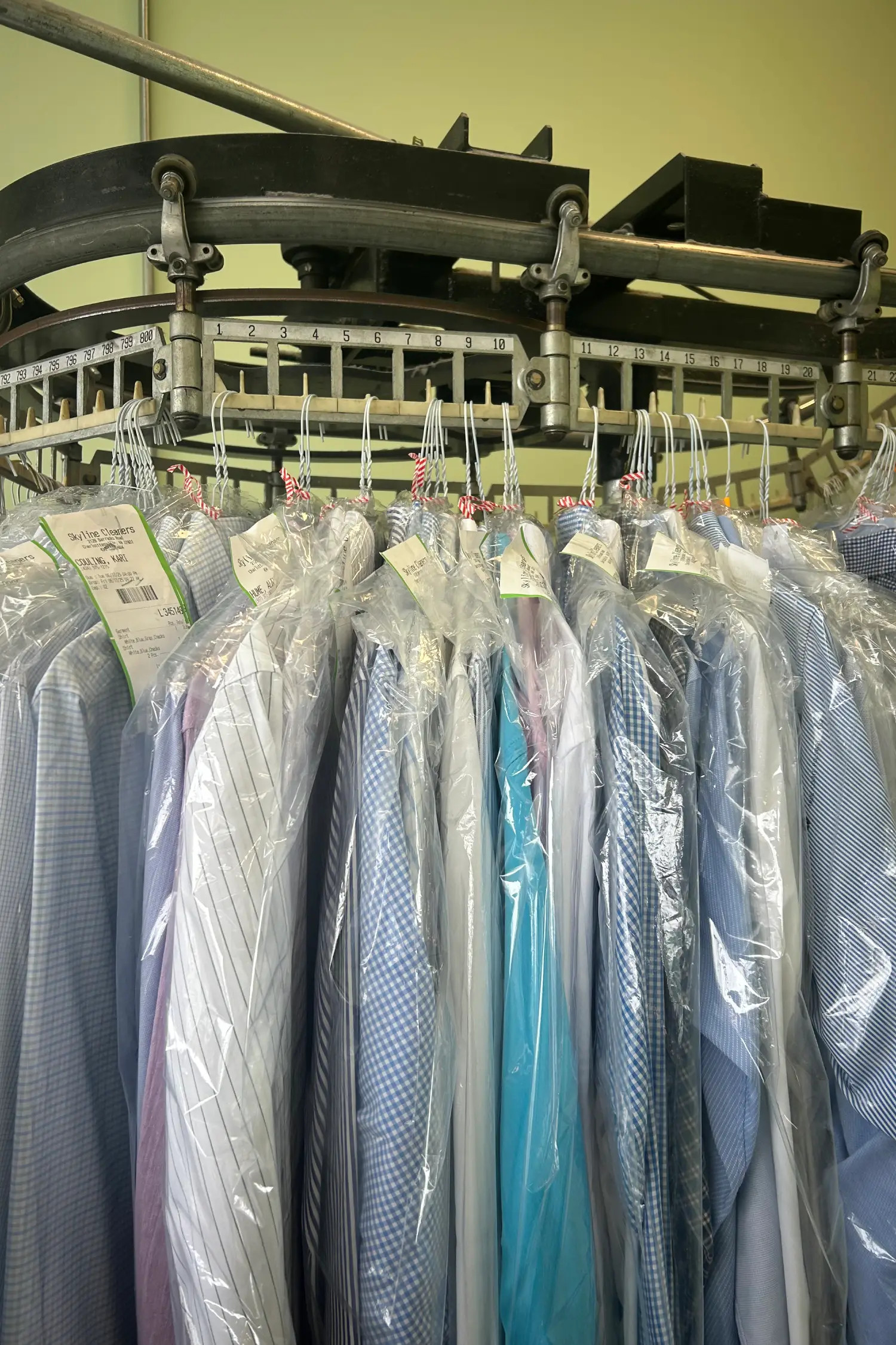 A row of neatly packaged, freshly cleaned dress shirts hanging on a rack in a dry cleaning facility.